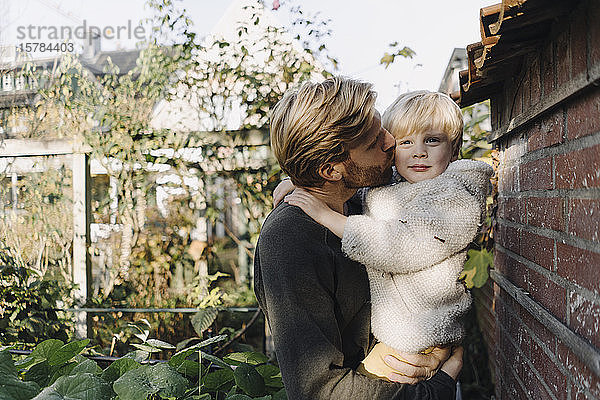 Vater hält und küsst Sohn im Garten