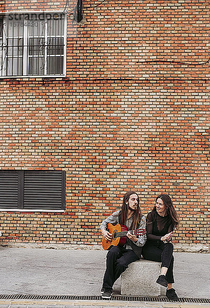 Zwei junge Musiker sitzen auf einem Stein und spielen Gitarre