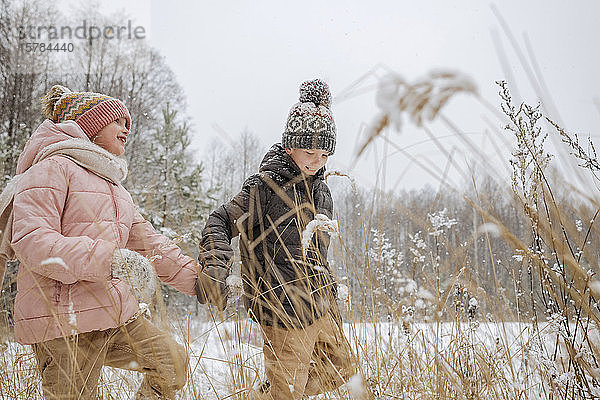 Zwei Geschwister gehen Hand in Hand im Winterwald