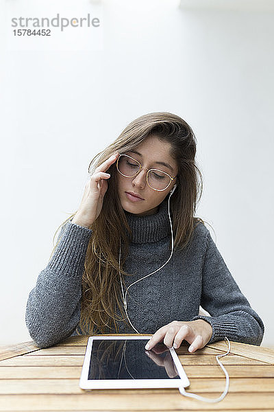 Porträt einer jungen Frau  die an einem Holztisch sitzt und Kopfhörer und digitales Tablett benutzt