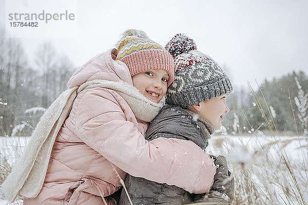 Junge reitet seine kleine Schwester huckepack im Winterwald