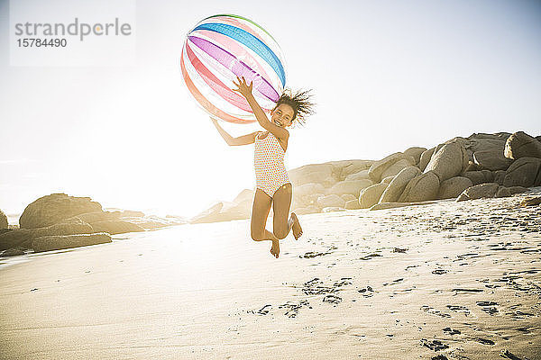 Glückliches Mädchen spielt mit aufblasbarem Ball am Strand