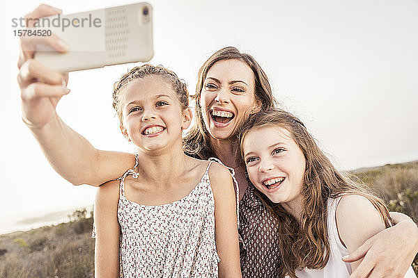 Glückliche Mutter  die mit ihren beiden Töchtern bei Sonnenuntergang ein Selfie macht