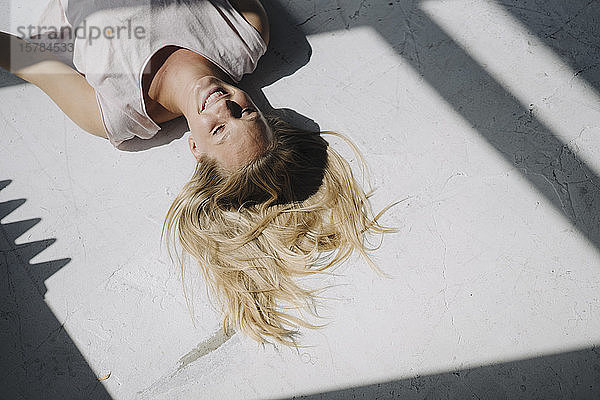 Lächelnde blonde junge Frau  die im Sonnenlicht auf dem Boden liegt
