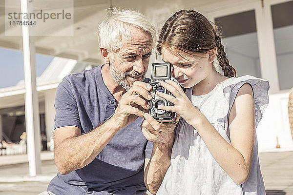 Vater und Tochter sitzen bei Sonnenschein auf der Terrasse und betrachten eine Oldtimer-Kamera