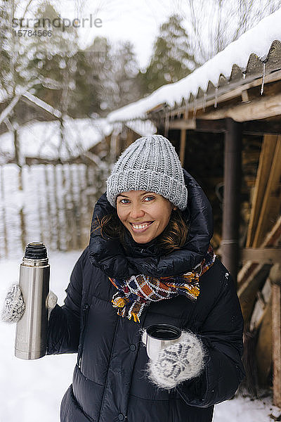 Porträt einer glücklichen Frau mit Thermoskanne im Winter