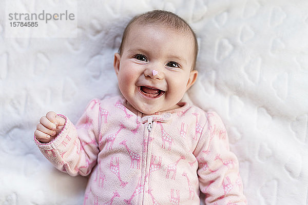 Porträt eines lachenden Mädchens mit rosa herzförmigen Bonbons auf der Nase
