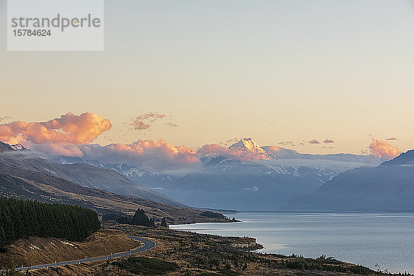 Neuseeland  Blick auf den neuseeländischen State Highway 80  der sich in der Morgendämmerung entlang des Ufers des Pukaki-Sees erstreckt  mit Mount Cook im Hintergrund