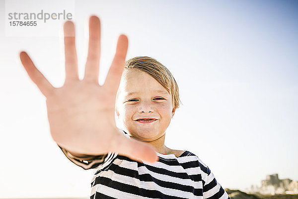 Porträt eines lächelnden Jungen  der seine Hand ausstreckt