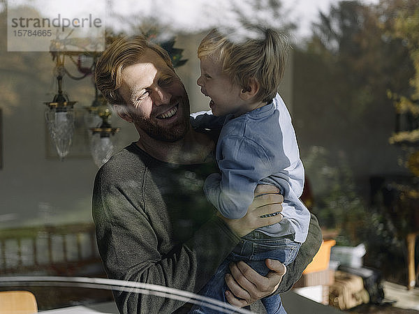 Glücklicher Vater trägt seinen Sohn zu Hause am Fenster