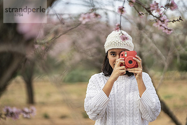 Porträt einer Teenagerin  die mit der Kamera zwischen blühenden Mandelbäumen fotografiert