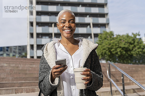 Stilvolle Geschäftsfrau  die mit Smartphone und Kaffeetasse durch die Stadt pendelt