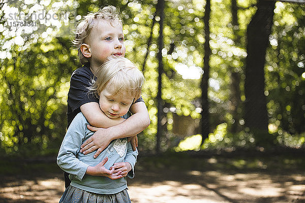 Junge umarmt seine kleine Schwester im Freien