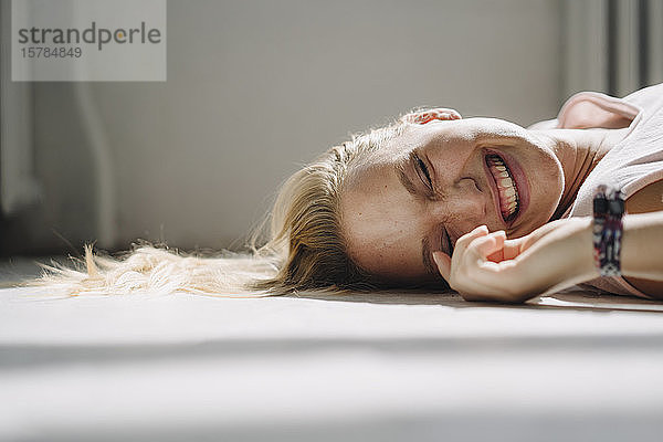 Porträt einer glücklichen blonden jungen Frau  die mit geschlossenen Augen auf dem Boden liegt