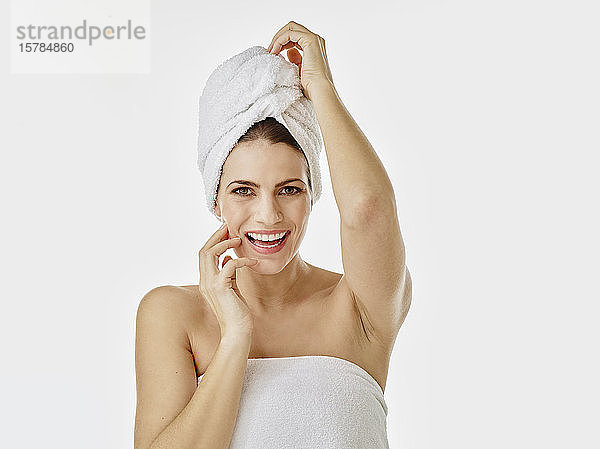 Bildnis einer glücklichen Frau mit in ein Handtuch gewickelten Haaren vor weißem Hintergrund