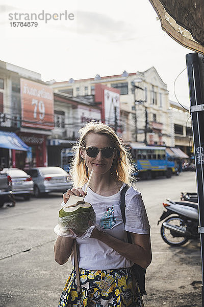 Porträt einer lächelnden Frau  die aus Kokosnuss trinkt  Altstadt Phuket  Thailand