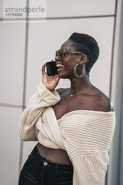 Porträt einer lachenden jungen Frau am Telefon mit Sonnenbrille