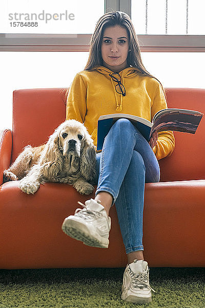 Porträt einer Teenagerin  die mit Hund und Buch auf der Couch sitzt