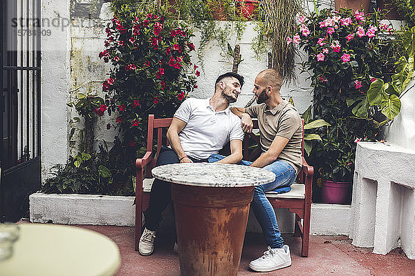 Schwules verliebtes Paar sitzt zusammen auf einer Bank auf einer Terrasse