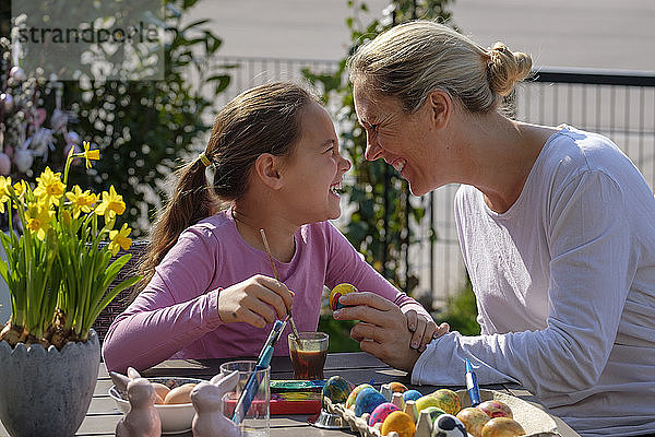Glückliche Mutter und Tochter malen Ostereier am Gartentisch und amüsieren sich