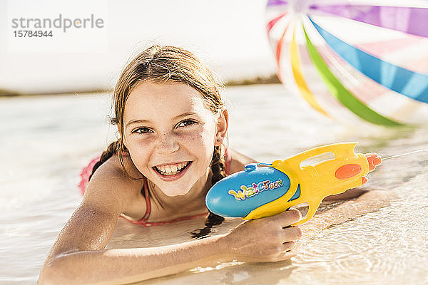 Porträt eines niedlichen Mädchens im Schwimmbad liegend mit Wasserpistole