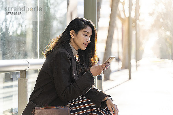 Junge Frau mit Smartphone an der Straßenbahnhaltestelle