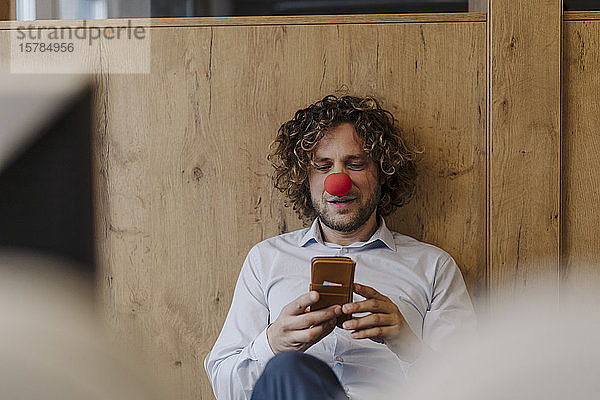 Geschäftsmann mit roter Clownsnase telefoniert im Büro