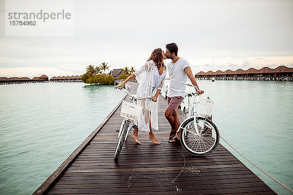 Paar mit Fahrrädern küsst sich auf einem Steg im Meer  Insel Maguhdhuvaa  Gaafu-Dhaalu-Atoll  Malediven
