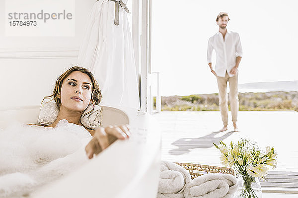 Junge Frau entspannt sich in Badewanne mit Mann im Hintergrund