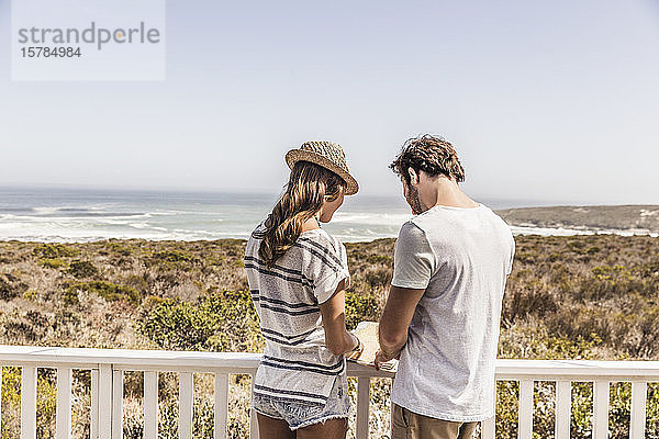 Rückansicht eines jungen Paares  das auf einer Terrasse am Meer steht