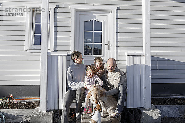 Glückliche Familie mit zwei Kindern und zwei Hunden  die vor ihrem Haus sitzen