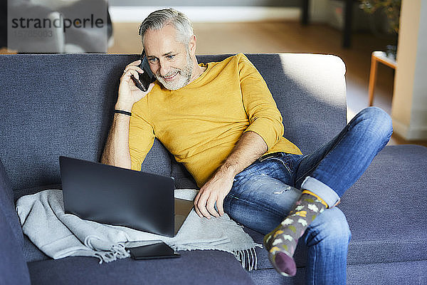 Erwachsener Mann benutzt Handy und Laptop zu Hause auf der Couch