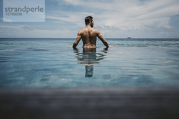 Rückansicht eines Mannes  der sich im Infinity-Pool entspannt  Insel Maguhdhuvaa  Gaafu-Dhaalu-Atoll  Malediven