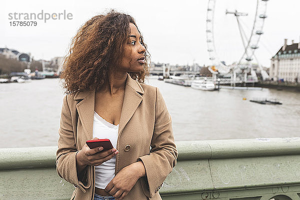 Junge Frau mit Handy in der Stadt und Lonon Eye im Hintergrund  London  Großbritannien