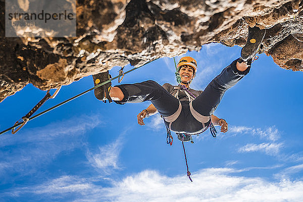 Porträt einer lächelnden Bergsteigerin  die sich von einer Felswand abseilt