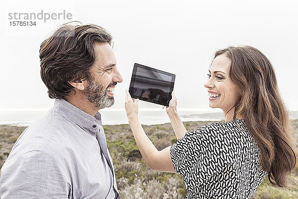 Glücklicher Mann sieht seine Frau mit Tablette in der Hand an der Küste
