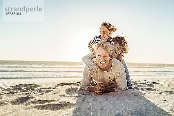 Vater amüsiert sich mit seinem Sohn am Strand  übereinander im Sand liegend