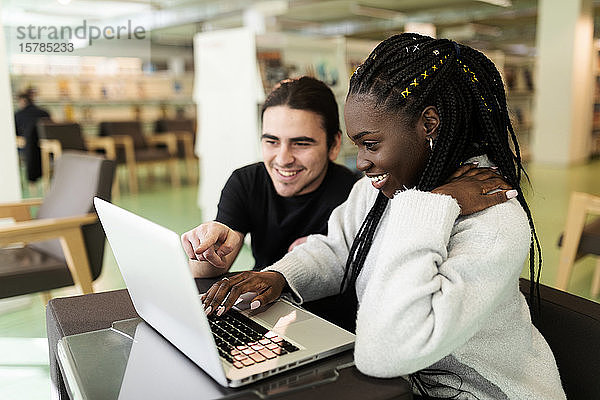 Zwei lächelnde Studenten mit Laptop in einer Bibliothek