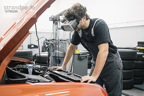 Automechaniker mit VR-Brille in einer Werkstatt bei der Arbeit am Auto