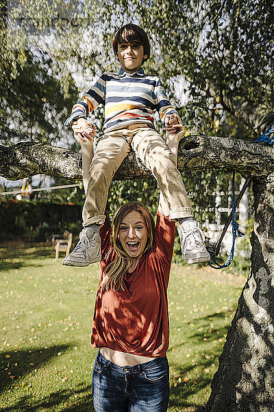 Junge klettert auf Baum  sitzt auf Ast  Mutter hält seine Hände