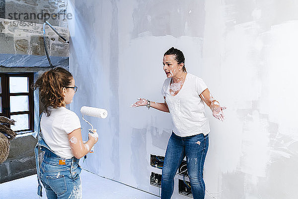 Mutter streitet mit ihrer Tochter  während sie eine Wand ihres neuen Hauses streicht