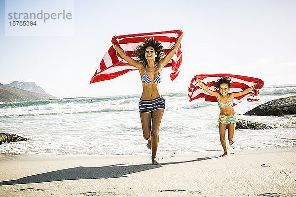 Glückliche Mutter und Tochter mit Handtüchern  die sich am Strand amüsieren