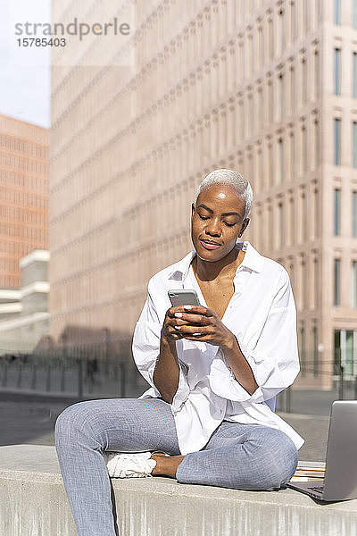 Geschäftsfrau  die in der Stadt sitzt und ein Smartphone benutzt