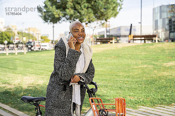 Geschäftsfrau  die mit ihrem Fahrrad in der Stadt pendelt und ein Smartphone benutzt
