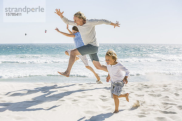 Vater amüsiert sich mit seinen Söhnen am Strand  rennt und springt im Sand