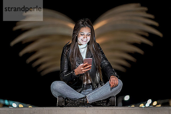 Porträt einer glücklichen Teenagerin  die nachts auf ein Smartphone schaut