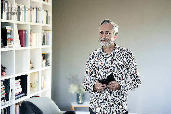 Reifer Mann mit Mobiltelefon  der zu Hause ein gemustertes Hemd trägt