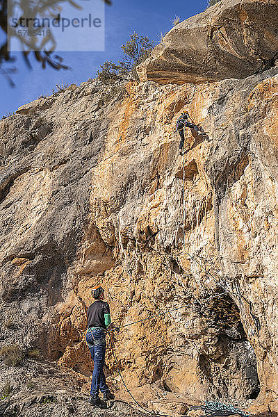 Mann sichert Frau beim Klettern an Felswand