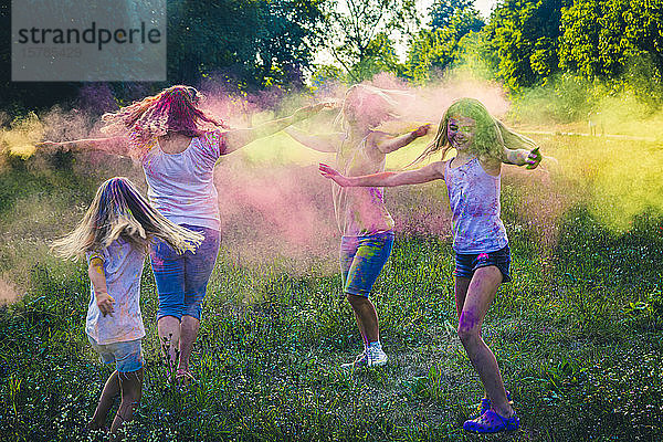 Gruppe von zwei Frauen und zwei Mädchen feiern das Fest der Farben auf einer Wiese