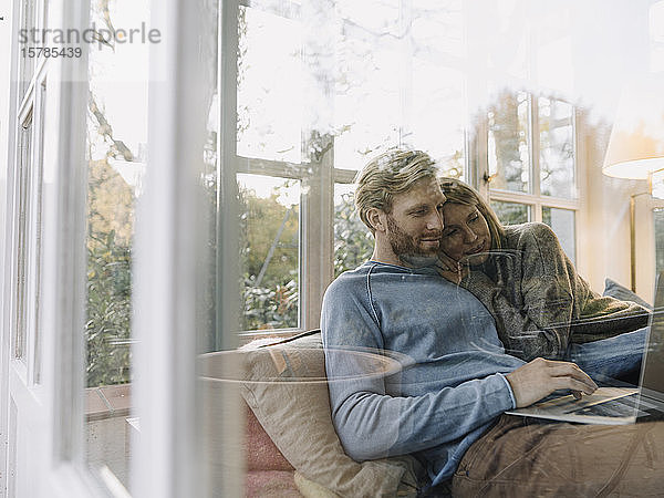 Mann und Frau benutzen zu Hause einen Laptop im Wintergarten